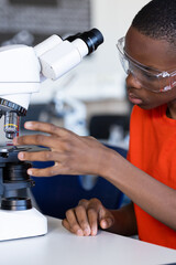 Using microscope, student conducting scientific experiment in school laboratory