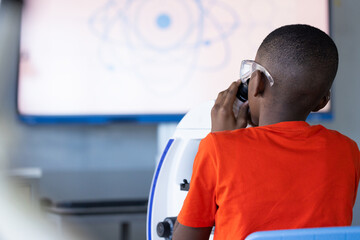 In school, boy using microscope for science experiment in classroom, copy space