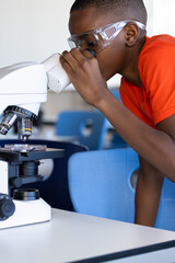 In school, boy using microscope and wearing safety goggles in science classroom
