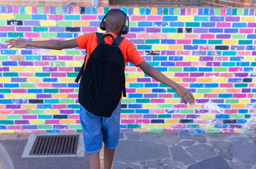 Wearing headphones, boy with backpack dancing in front of colorful school wall © WavebreakMediaMicro