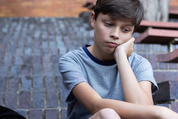 Sitting on steps, boy looking thoughtful and pensive after school day