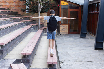 Fototapeta premium Balancing on bench, boy with backpack enjoying outdoor activity at school