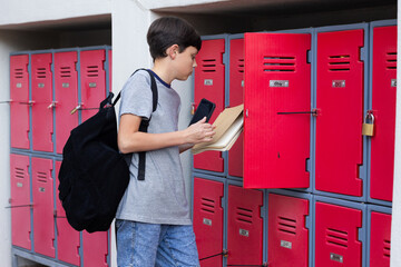 Opening locker, boy with backpack holding books and smartphone at school, copy space