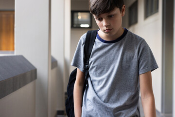 Walking in school hallway, boy with backpack looking down, feeling sad