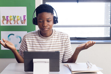 Using tablet and wearing headphones, student studying in school with recycle posters