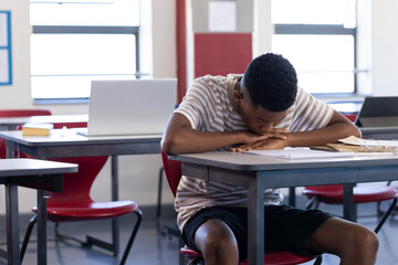 In school, boy resting head on desk in classroom, looking tired