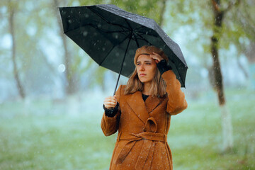 Woman Holding an Umbrella while it Snows in Spring. Unhappy lady suffering in a bad springtime...