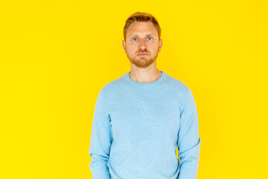 Studio portrait of a serious young red-haired man standing against a vibrant yellow backdrop