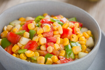 Colorful vegetable salad made of tomato, green pepper, cucumber and corn kernels, served in bowl (Selective Focus, Focus in the middle of the image) 
