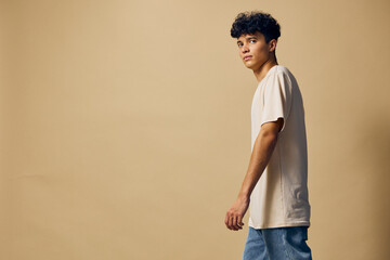Young man in casual outfit walking against a plain beige background, showcasing modern fashion...