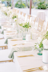 Long set festive table with bouquets of flowers, transparent crockery and candles