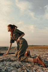 Woman in green jumpsuit crouching on rock in field, adventure and nature exploration concept