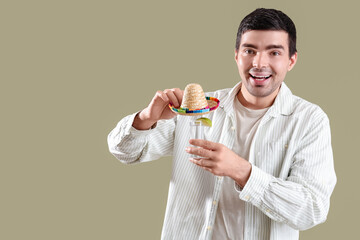 Young man with tequila shot and sombrero hat on green background