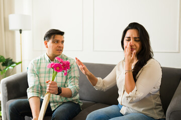 Allergic woman covering nose, wincing from strong gerbera fragrance, pushing away pink flowers...