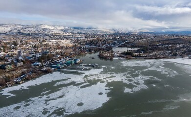 Aerial view of a partially frozen lake Klamath Falls, Oregon, USA, with a marina and a town nestled against snow-covered mountains in the background. Winter landscape.