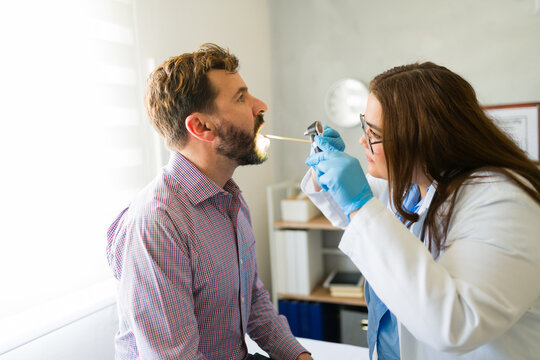 Medical professional wearing protective gloves checking male patient's throat during routine healthcare examination in clinical setting