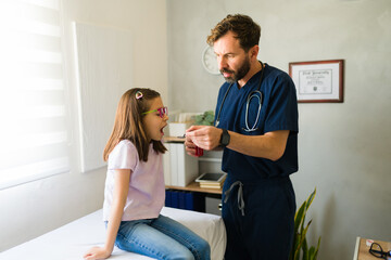 Caring pediatrician giving syrup medicine to a little girl patient during a medical check up in the...