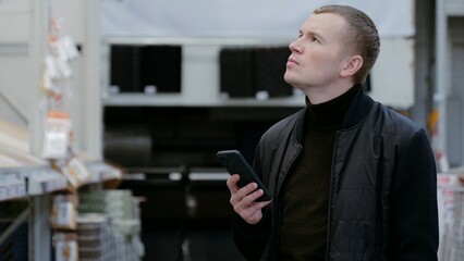A man in a hardware store, choosing flooring, shelves with ceramic tiles. Customer shopping for...