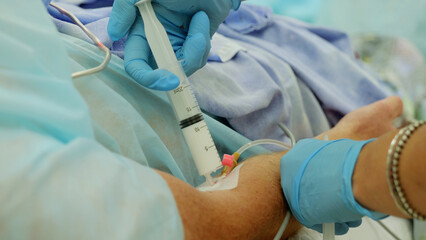 Nurse wearing blue surgical gloves is injecting medicine into a catheter in a patient's arm during a medical procedure