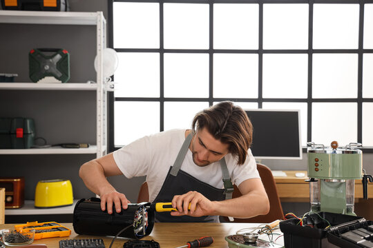 Male worker with screwdriver repairing coffee machine at table in workshop