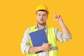 Male contractor with clipboard pointing at something on yellow background