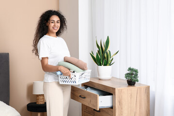 Beautiful young happy African-American woman putting clean clothes into commode at home