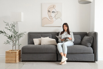 Young woman reading magazine on black sofa in living room