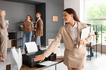 Young businesswoman with laptop using printer in office