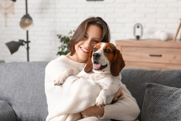 Young woman hugging adorable Beagle dog on comfortable sofa at home