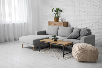 Comfortable sofa with cushion, pouf and coffee table in interior of living room