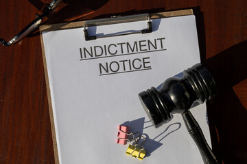 A formal indictment notice paper secured in a clipboard, set alongside a gavel on the desk,...
