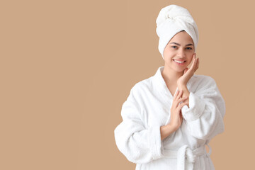 Beautiful young happy woman in bathrobe with towel on beige background