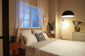 Comfortable bed with glowing lamps in interior of modern bedroom