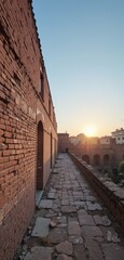 A rustic brick wall stands prominently in the foreground, its weathered texture illuminated by the warm, golden hues of a breathtaking sunset, casting long shadows and creating a serene atmosphere.