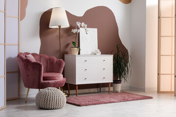 Obraz premium Armchair, chest of drawers, lamp and pouf in interior of living room