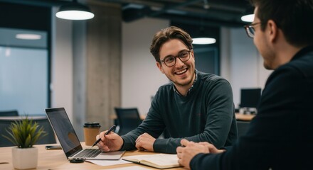 Two young businessmen collaborating on project using laptop in office space