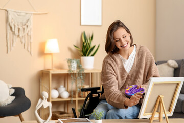 Young pretty woman in wheelchair painting picture at home