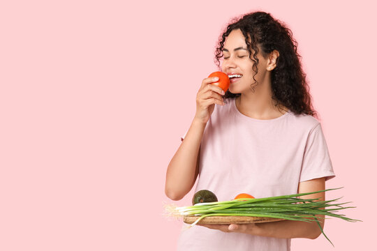 Young happy African-American woman with board of different fresh vegetables on pink background. Independence from Meat Day
