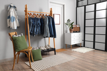 Rack with stylish denim clothes near white wall in room