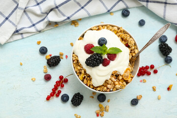 Napkin, bowl of tasty granola with yogurt and berries on pale blue background