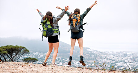 Women, hiking and jump on mountain, celebration and achievement at summit with goals in nature. People, girl and friends with cheers, success and trail with back, cityscape and adventure in Italy © peopleimages.com
