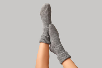 Legs of young woman in warm knitted socks on grey background
