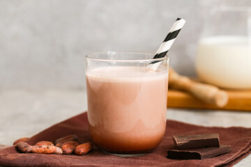 Glass of sweet chocolate milk and cocoa beans on grey background