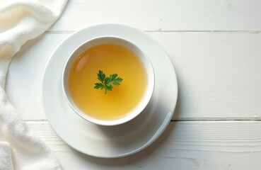 Top view chicken broth bowl with fresh parsley leaf, white plate on a table. Homemade healthy bone broth for cooking and diet. Tasty meal, soup ingredient.