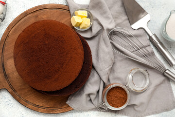 Wooden board with sponge cake layers, cocoa powder, butter, utensils and napkin on light background