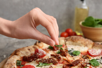 Hand of woman sprinkling tasty pizza with cheese on grey background, closeup