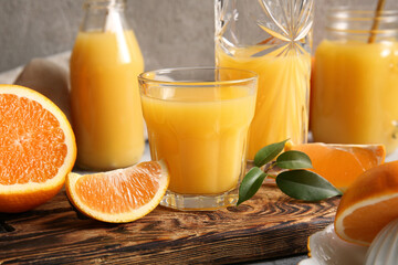 Glasses and bottle of fresh orange juice with fruits on grey background