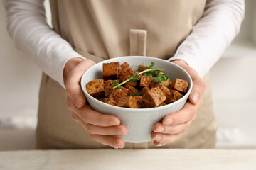 Woman holding bowl with pieces of fried tofu cheese and micro green in kitchen