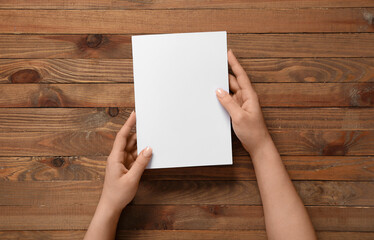 Female hands with blank brochure on wooden background