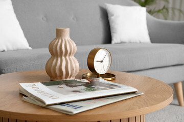 Stylish coffee table with magazines, vase and alarm clock in living room, closeup